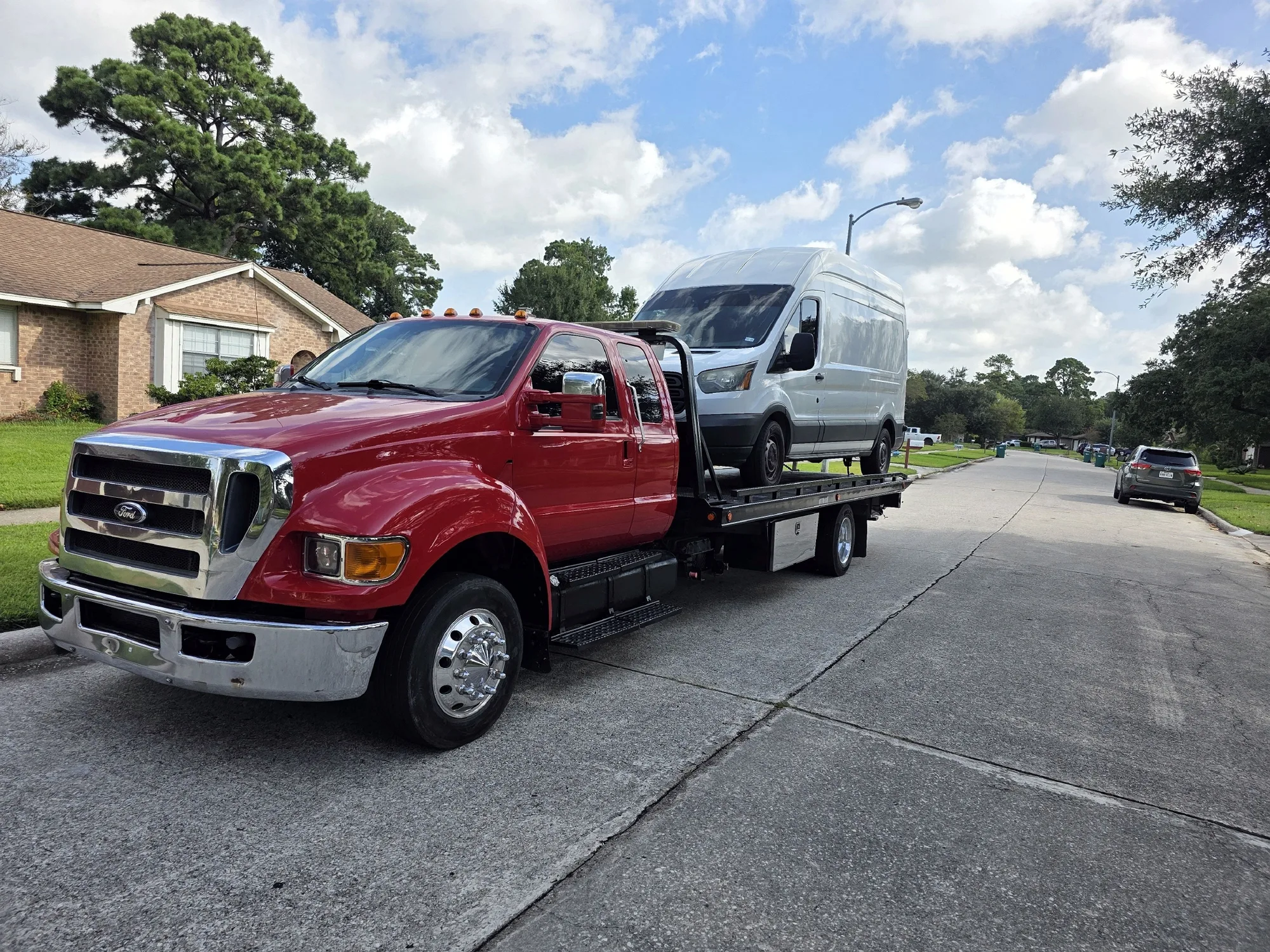 DMC flatbed tow truck carrying a white cargo van on a Spring, TX neighborhood street
